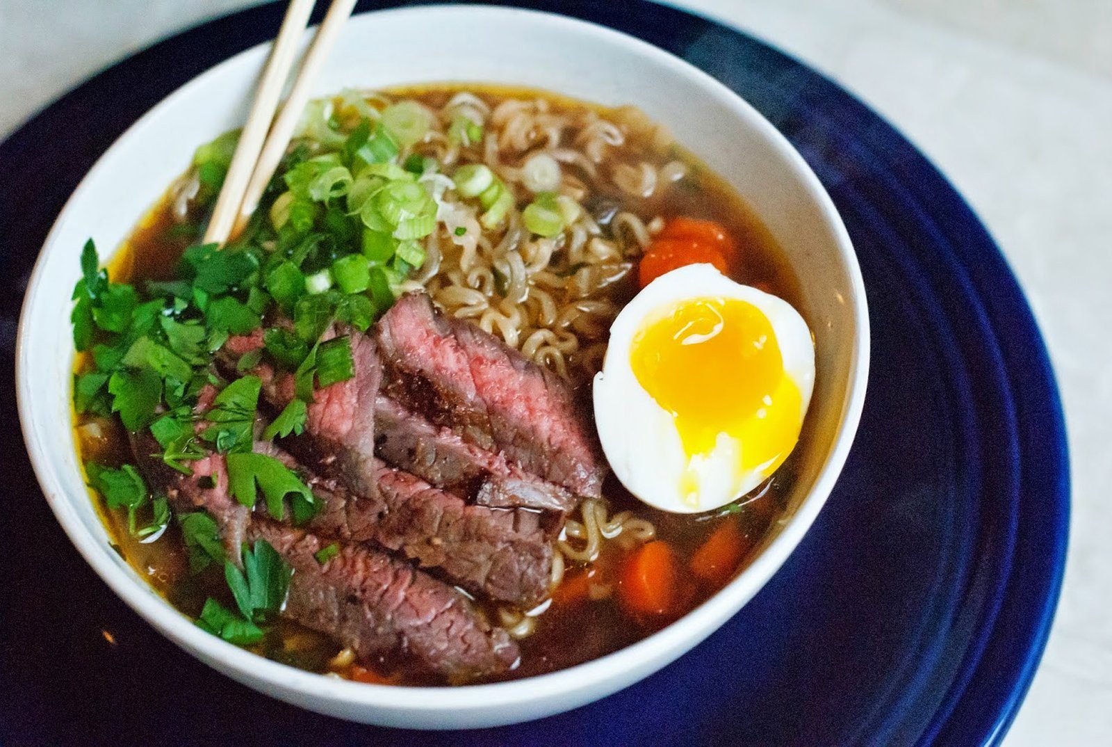 A bowl of ramen with sliced beef, soft egg and scallions