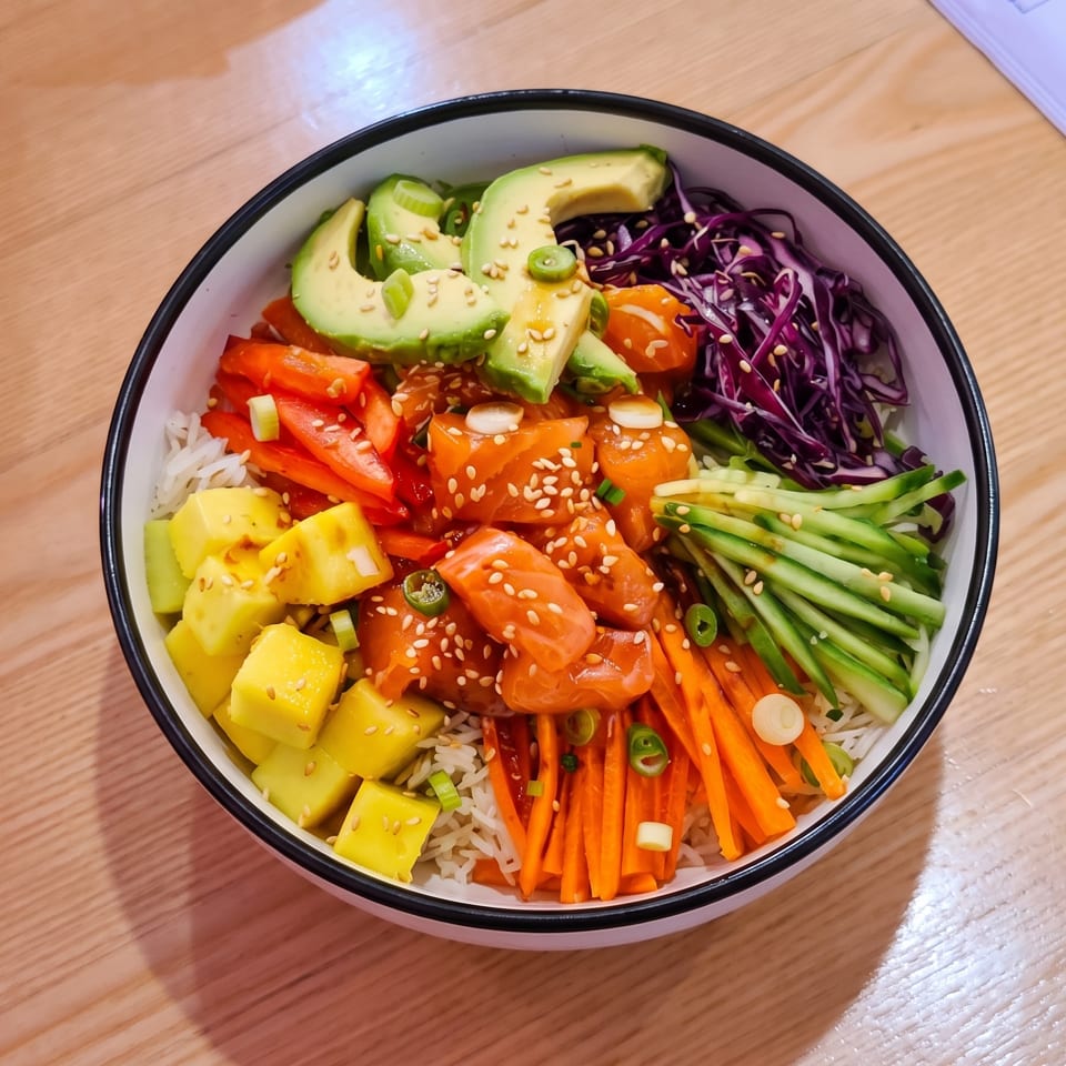 Colorful poke bowl with salmon, avocado, mango, carrots, cucumber, and red cabbage on rice.