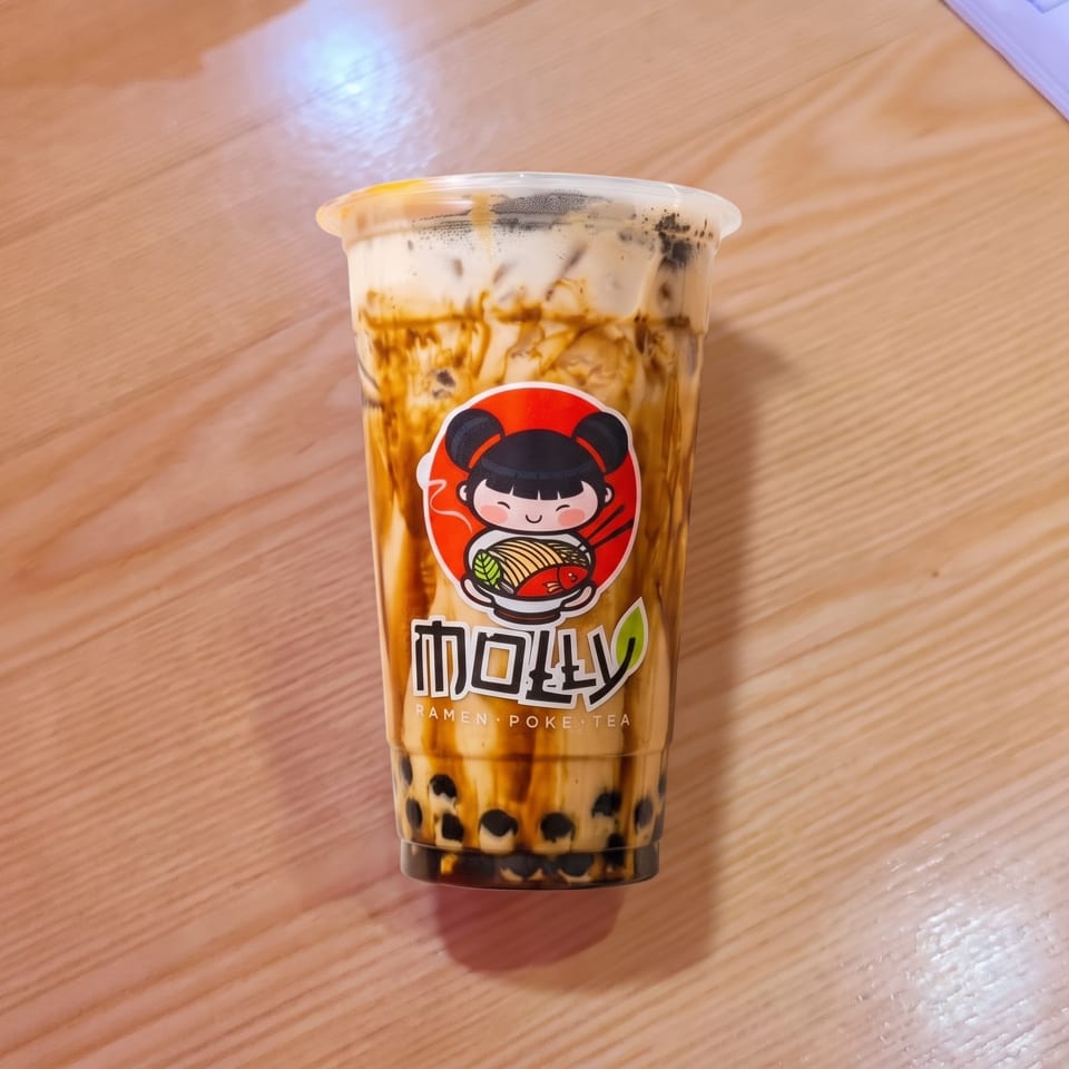A Molly Ramen Poke Tea bubble tea with brown sugar streaks and tapioca pearls on a wooden table.
